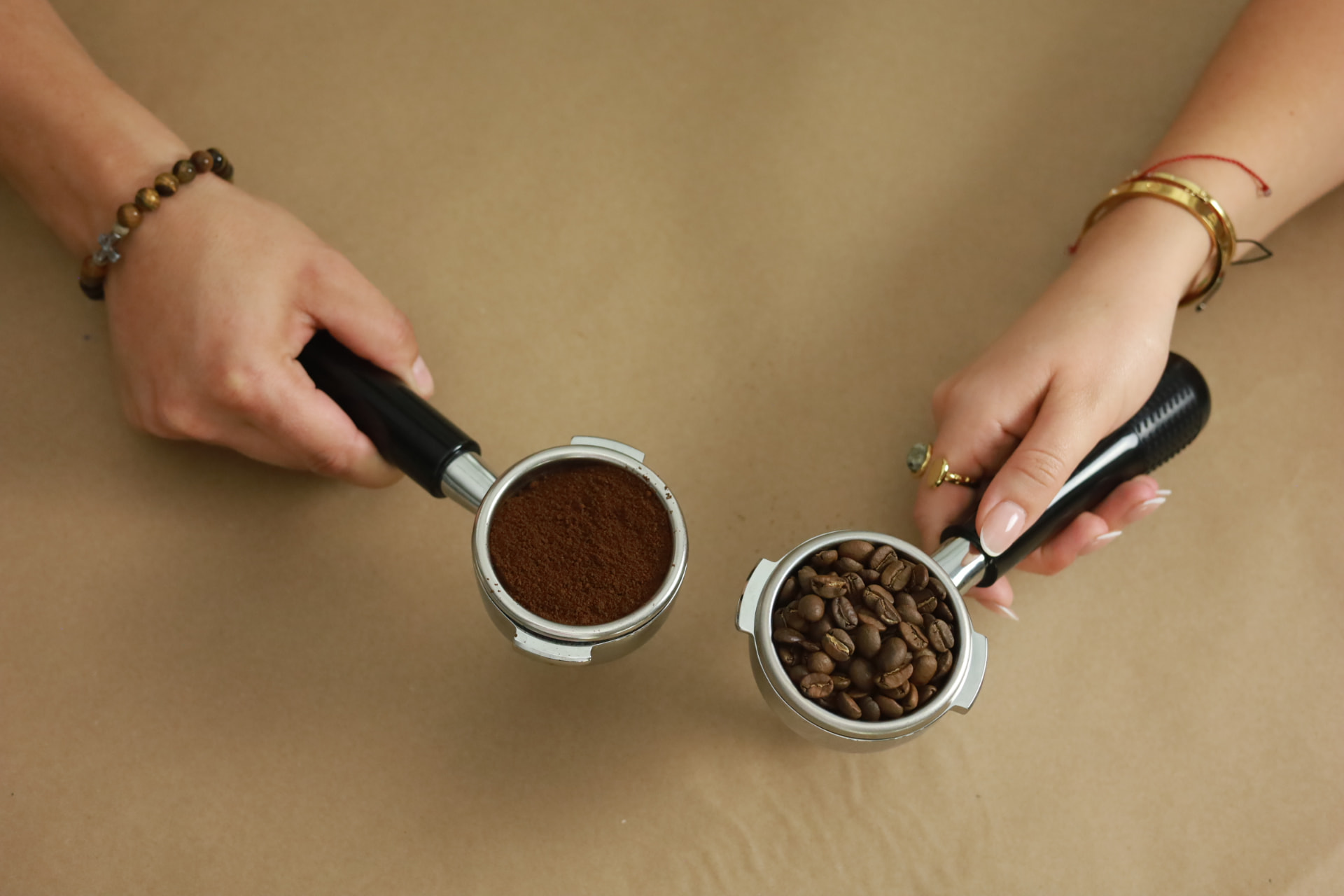 Two portafilters held over a warm wooden surface — one with freshly ground espresso, one with whole Peruvian coffee beans